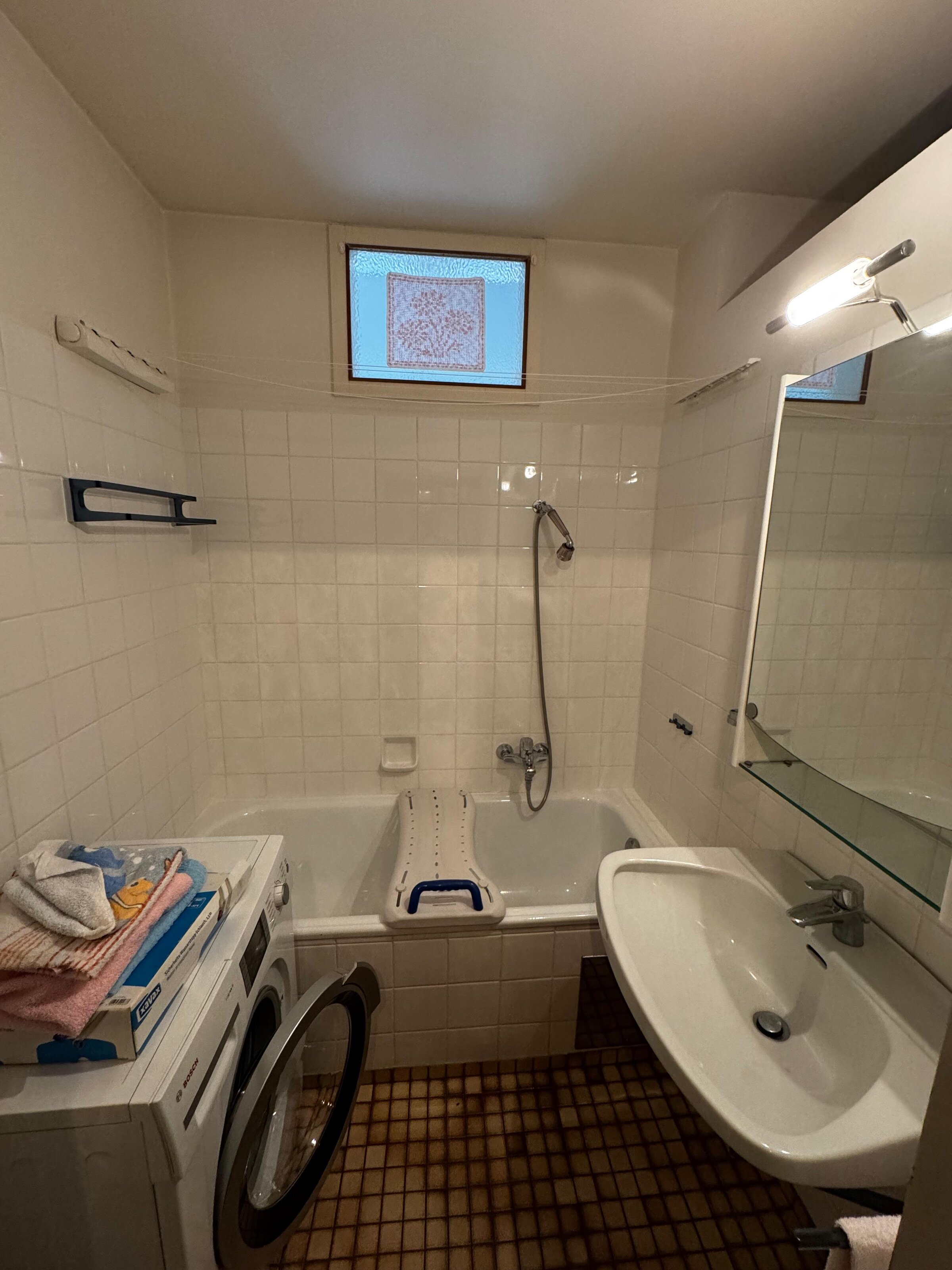 Das Badezimmer ist mit einer Badewanne mit Duschfunktion ausgestattet. Helle weiße Fliesen sorgen für eine freundliche Atmosphäre. Waschbecken mit Spiegel und Ablage für zusätzlichen Komfort. Auch eine Waschmaschine ist vorhanden | © Stefan Gabriel