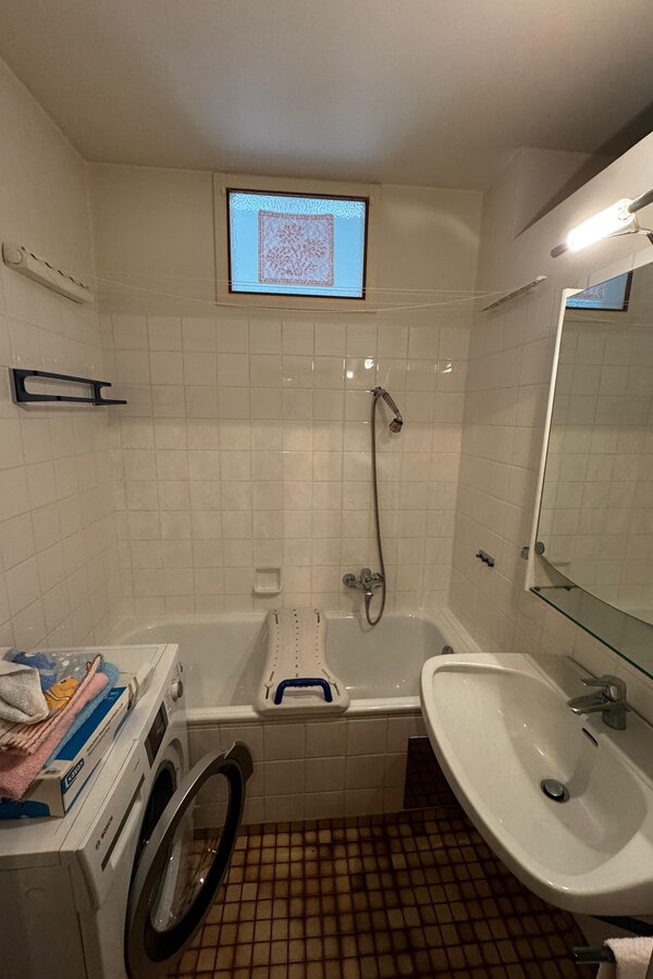 Das Badezimmer ist mit einer Badewanne mit Duschfunktion ausgestattet. Helle weiße Fliesen sorgen für eine freundliche Atmosphäre. Waschbecken mit Spiegel und Ablage für zusätzlichen Komfort. Auch eine Waschmaschine ist vorhanden | © Stefan Gabriel