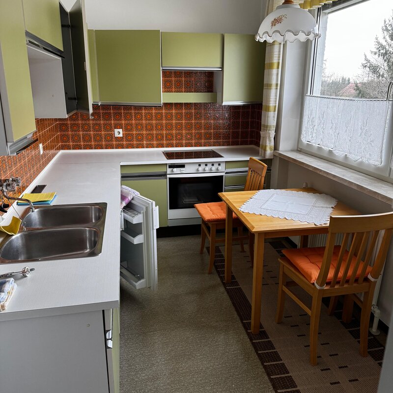 Die Küche ist voll ausgestattet und bietet ausreichend Arbeitsfläche. Der Essbereich mit Tisch und zwei Stühlen liegt direkt am Fenster und sorgt für eine helle, freundliche Atmosphäre. Die Einbauküche verfügt über Backofen, Herd, Spüle und Kühlschrank. Klassische Fliesen verleihen der Küche einen charmanten Retro-Stil. | © Stefan Gabriel