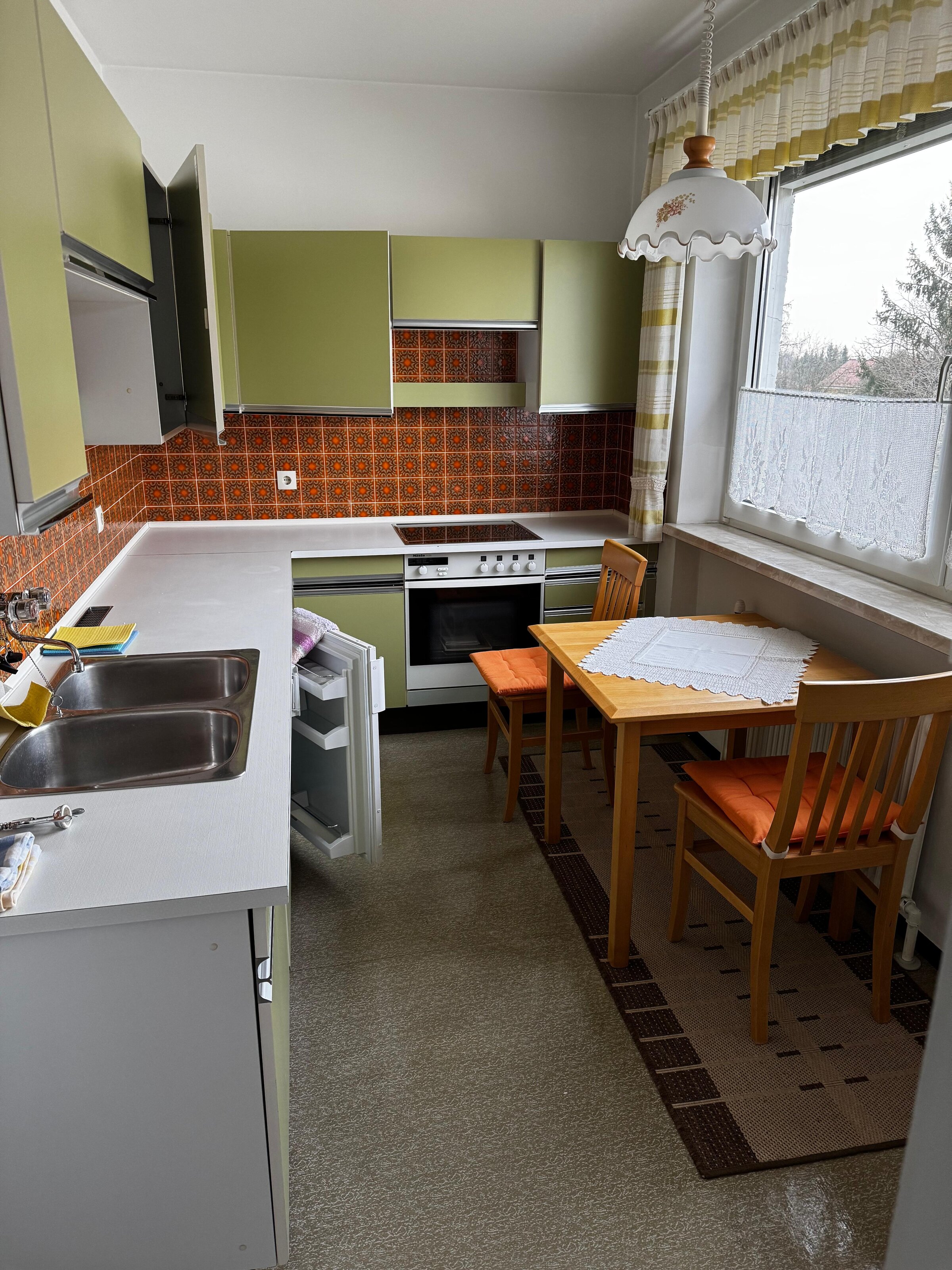 Die Küche ist voll ausgestattet und bietet ausreichend Arbeitsfläche. Der Essbereich mit Tisch und zwei Stühlen liegt direkt am Fenster und sorgt für eine helle, freundliche Atmosphäre. Die Einbauküche verfügt über Backofen, Herd, Spüle und Kühlschrank. Klassische Fliesen verleihen der Küche einen charmanten Retro-Stil. | © Stefan Gabriel