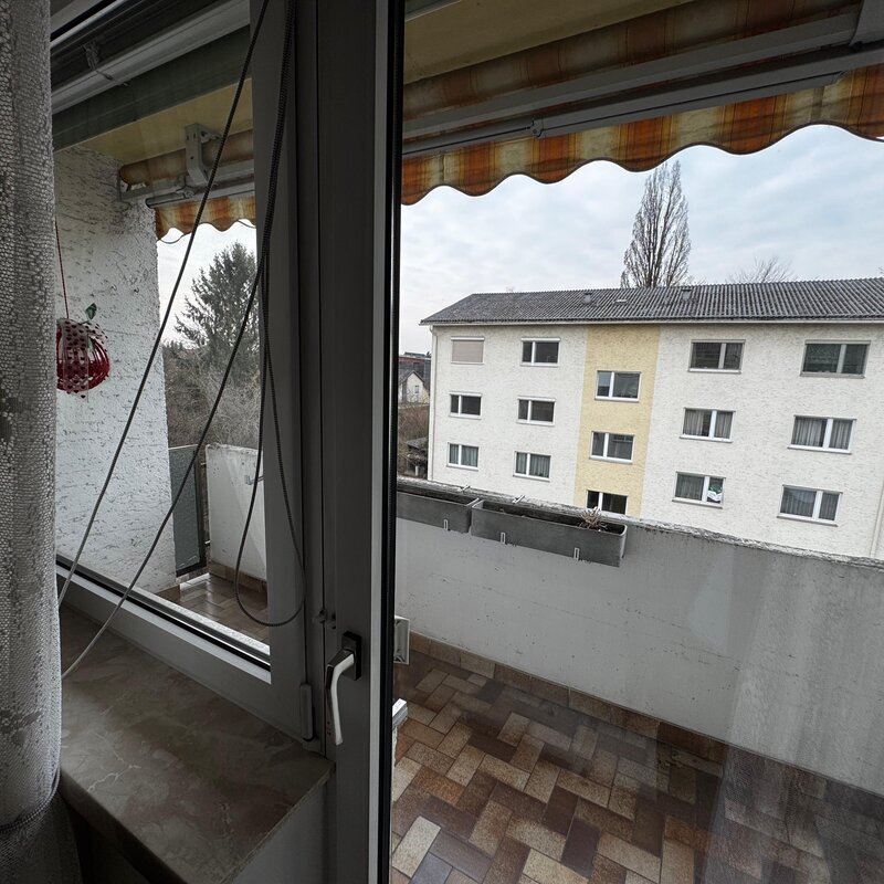 Die 6 m² große Loggia bietet einen schönen Ausblick auf die umliegenden Wohnhäuser und Grünflächen. Große Fenster lassen viel Tageslicht in die Wohnung. Ein Sonnenschutz-Markise sorgt für angenehmen Schatten an heißen Tagen. Die Loggia ist ideal zum Entspannen und bietet zusätzlichen Wohnraum im Freien. | © Stefan Gabriel