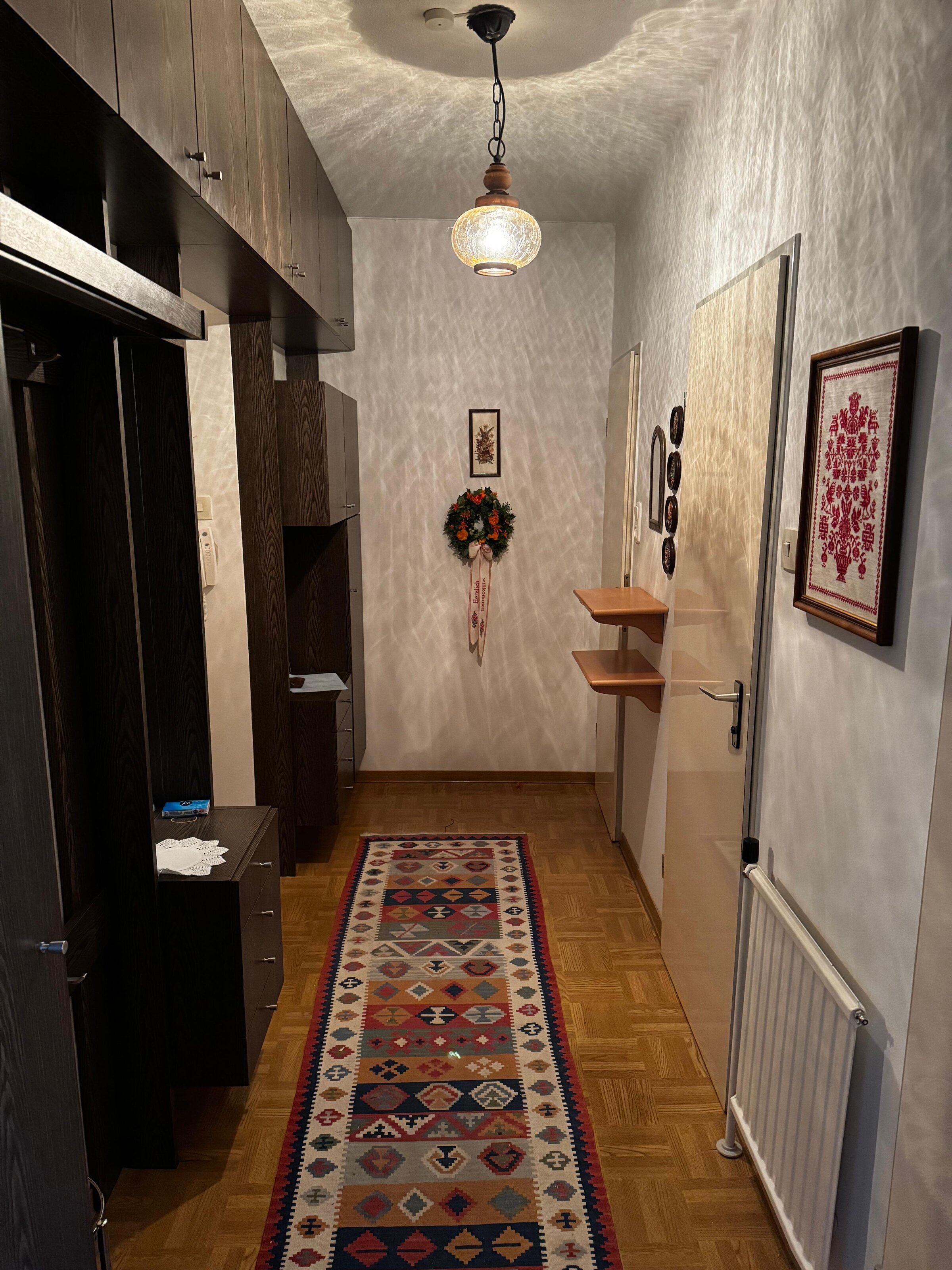 Der Vorraum bietet eine praktische Garderobe mit Ablagemöglichkeiten und ausreichend Platz für Jacken und Schuhe. Die Wanddekoration und der Teppich verleihen dem Eingangsbereich eine gemütliche Atmosphäre. Von hier aus gelangt man in die weiteren Räume der Wohnung. | © Stefan Gabriel