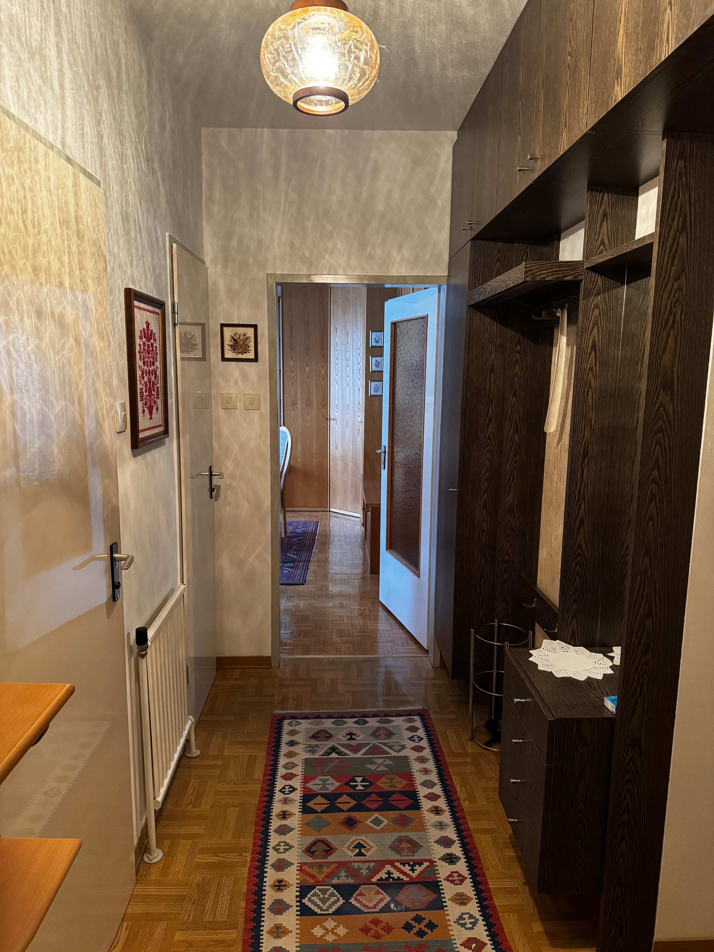 Der Vorraum bietet eine praktische Garderobe mit Stauraum und eine helle Atmosphäre. Von hier aus gelangt man in das Wohn-/Schlafzimmer, das durch eine offene Tür sichtbar ist. Die Kombination aus Holzmöbeln und Wanddekoration verleiht dem Eingangsbereich einen gemütlichen Charakter. | © Stefan Gabriel