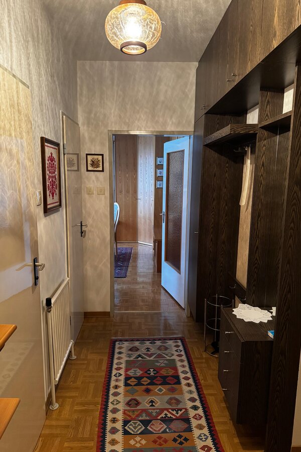 Der Vorraum bietet eine praktische Garderobe mit Stauraum und eine helle Atmosphäre. Von hier aus gelangt man in das Wohn-/Schlafzimmer, das durch eine offene Tür sichtbar ist. Die Kombination aus Holzmöbeln und Wanddekoration verleiht dem Eingangsbereich einen gemütlichen Charakter. | © Stefan Gabriel