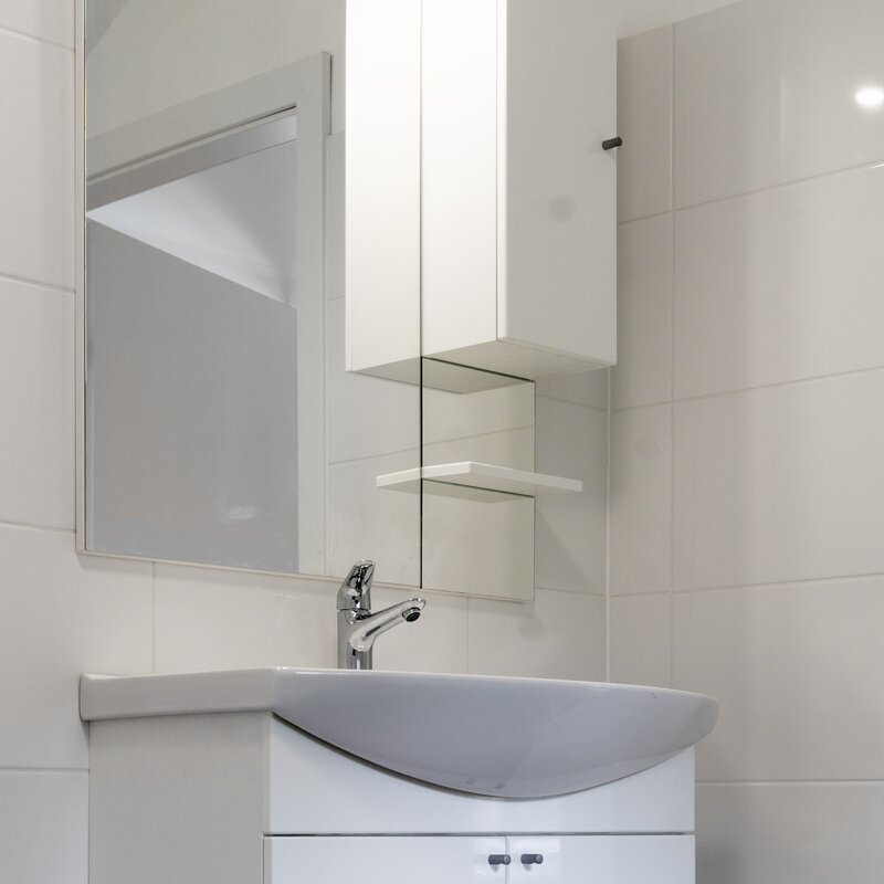 Above the vanity unit there is a big mirror beside an upper side cabinet with a one-pece shelf on the right.