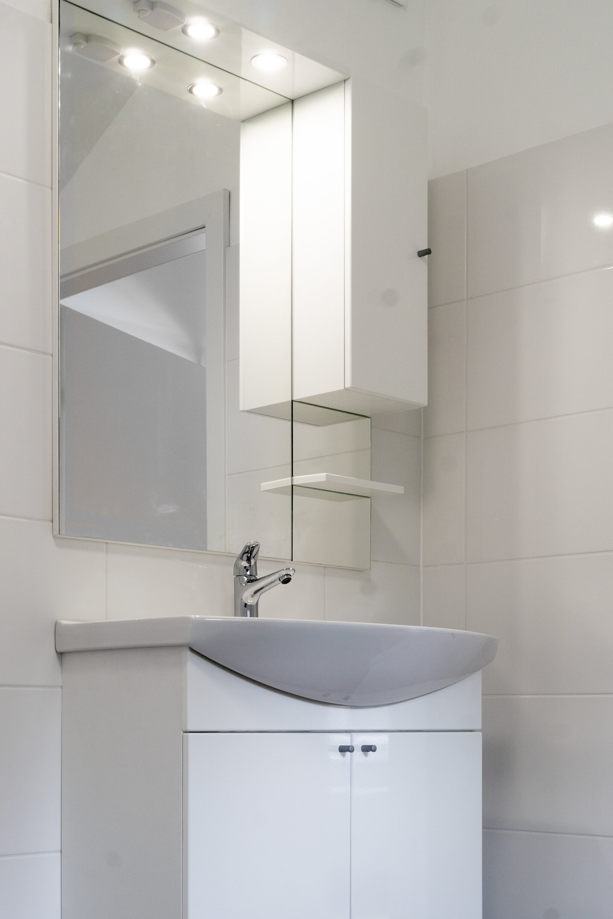 Above the vanity unit there is a big mirror beside an upper side cabinet with a one-pece shelf on the right.