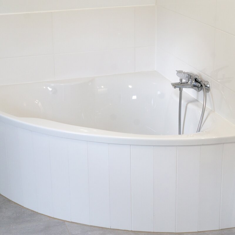 Rechts schmiegt sich eine Eckbadewanne platzsparend in das geräumige Badezimmer, in dem sich auf der gegenüberliegenden Seite auch eine Waschmaschine und ein gartenseitiges Fenster befinden..