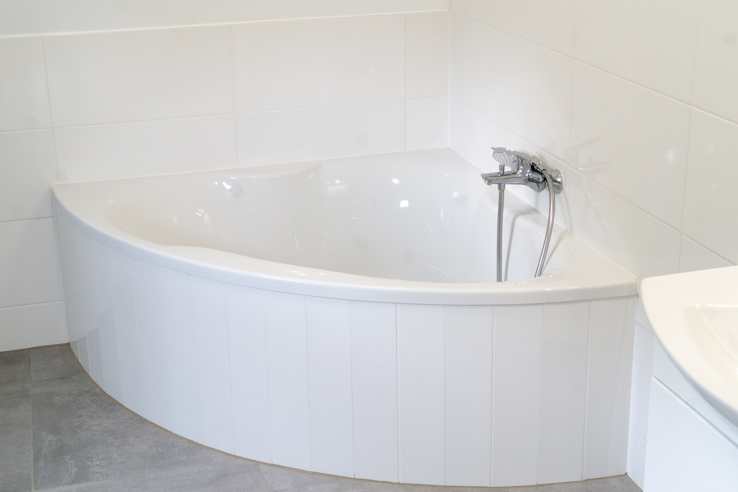 Rechts schmiegt sich eine Eckbadewanne platzsparend in das geräumige Badezimmer, in dem sich auf der gegenüberliegenden Seite auch eine Waschmaschine und ein gartenseitiges Fenster befinden..
