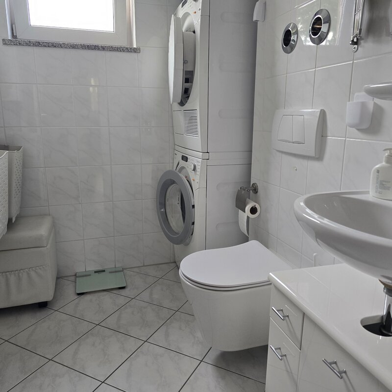 Dieses praktische zweite Badezimmer ist mit einem WC, Waschbecken und einem Waschmaschinen-Trockner-Turm ausgestattet. Ideal für Familien oder Wohngemeinschaften - hier lassen sich Wäschepflege und tägliche Nutzung bequem kombinieren. Helle Fliesen, Tageslichtfenster und durchdachte Stauraumlösungen sorgen für Funktionalität und Komfort.