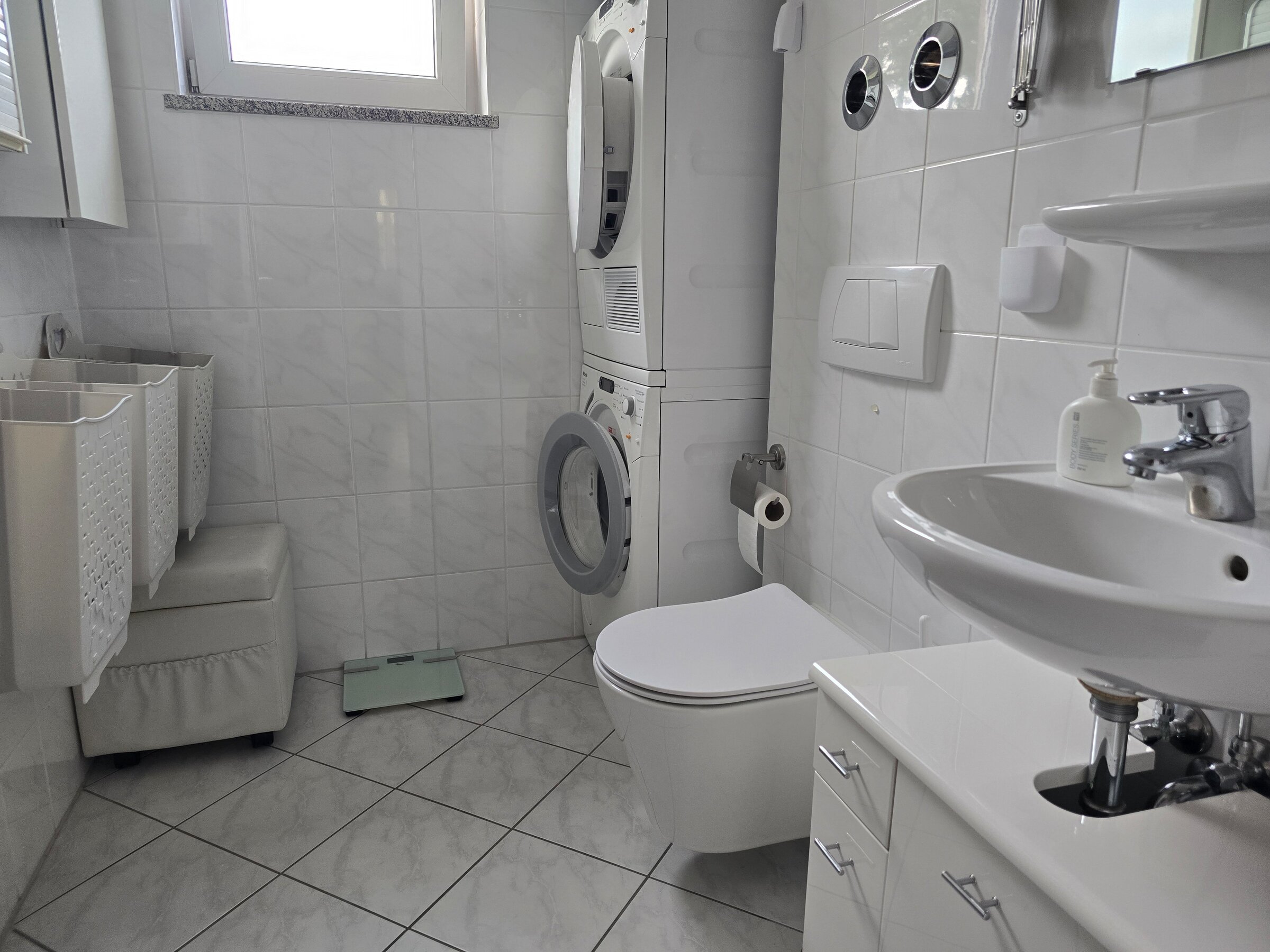 Dieses praktische zweite Badezimmer ist mit einem WC, Waschbecken und einem Waschmaschinen-Trockner-Turm ausgestattet. Ideal für Familien oder Wohngemeinschaften - hier lassen sich Wäschepflege und tägliche Nutzung bequem kombinieren. Helle Fliesen, Tageslichtfenster und durchdachte Stauraumlösungen sorgen für Funktionalität und Komfort.