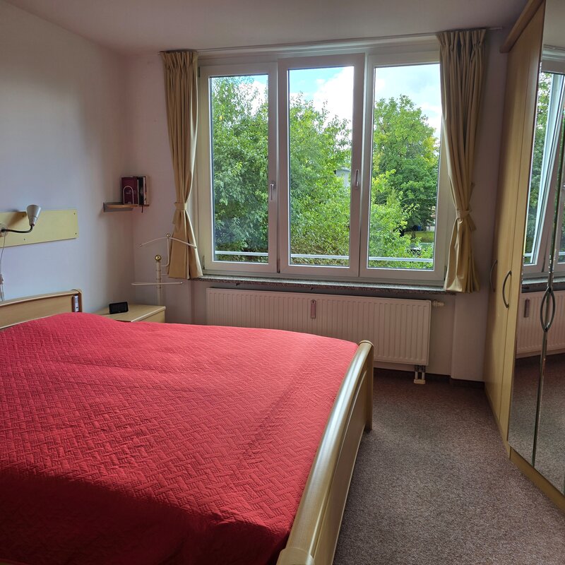 Das Schlafzimmer verfügt über ein großes Fenster auf der Westseite mit viel Tageslicht und Naturblick. Der raumhohe Einbauschrank mit Spiegelfront bietet großzügigen Stauraum und lässt den Raum größer wirken.