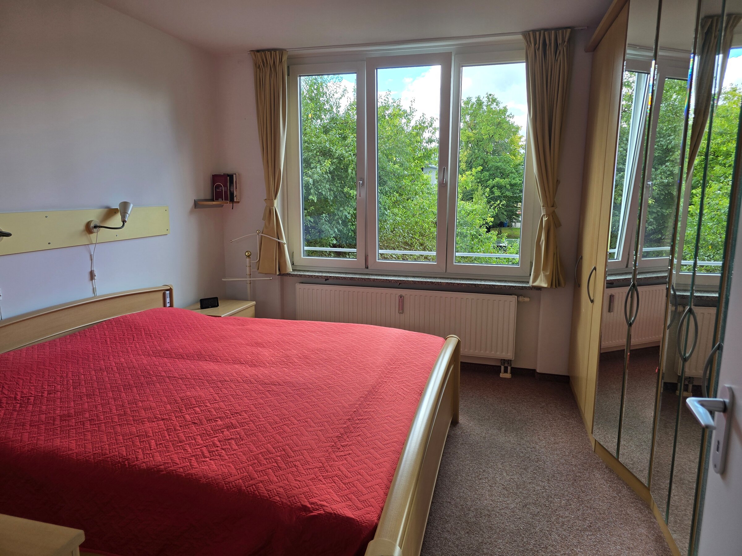 Das Schlafzimmer verfügt über ein großes Fenster auf der Westseite mit viel Tageslicht und Naturblick. Der raumhohe Einbauschrank mit Spiegelfront bietet großzügigen Stauraum und lässt den Raum größer wirken.