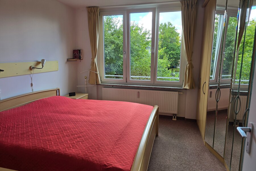 Das Schlafzimmer verfügt über ein großes Fenster auf der Westseite mit viel Tageslicht und Naturblick. Der raumhohe Einbauschrank mit Spiegelfront bietet großzügigen Stauraum und lässt den Raum größer wirken.