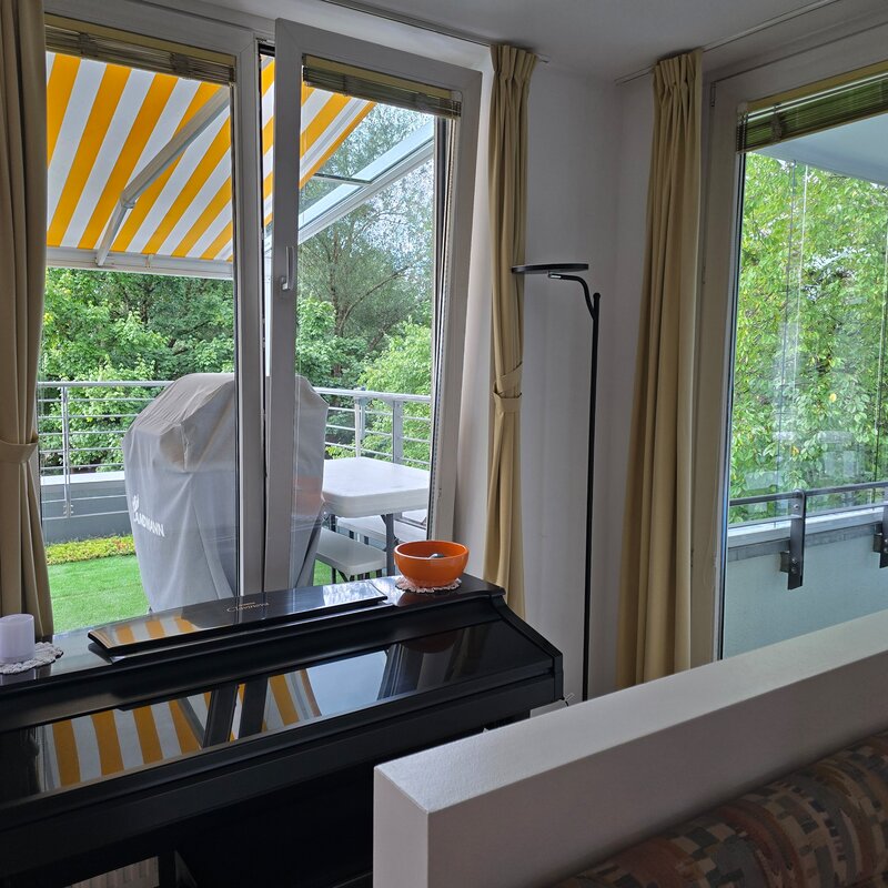 Der Blick vom Essbereich zeigt drei bodentiefe Fenster bzw. Türen nach außen: Links die Terrassentür, in der Mitte ein weiteres Fenster zur Terrasse und ganz rechts die Tür zur verglasten Loggia mit Blick ins Grüne.