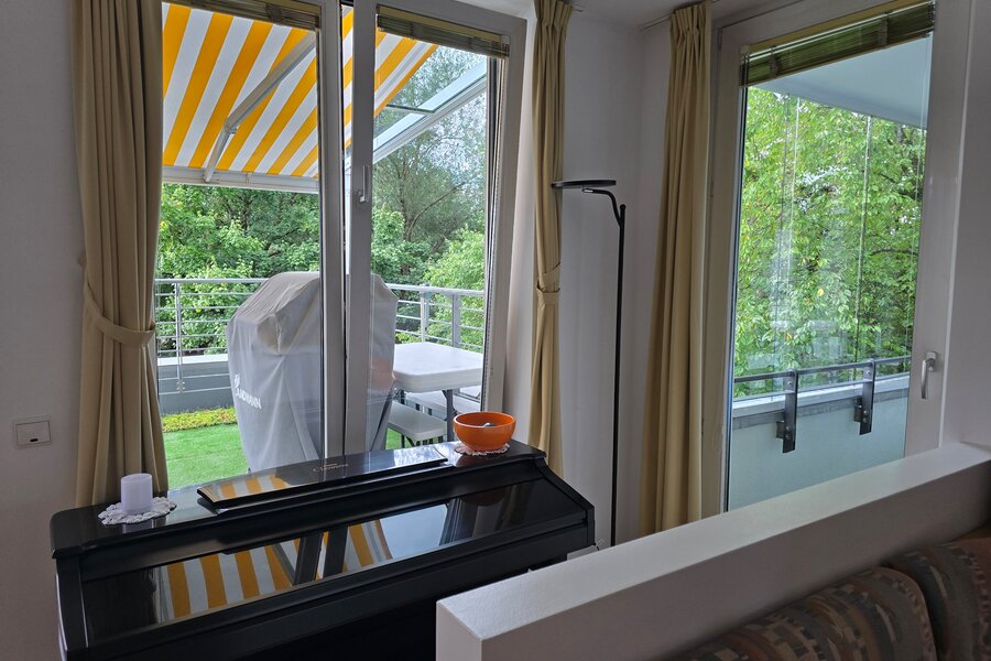 Der Blick vom Essbereich zeigt drei bodentiefe Fenster bzw. Türen nach außen: Links die Terrassentür, in der Mitte ein weiteres Fenster zur Terrasse und ganz rechts die Tür zur verglasten Loggia mit Blick ins Grüne.