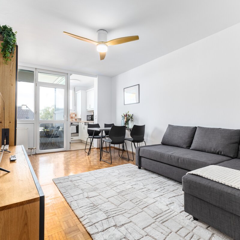 Helles, modern eingerichtetes Wohnzimmer mit gemütlichem Sofa, Essbereich und direktem Zugang zur Küche. Große Fenster sorgen für viel Tageslicht und eine freundliche Atmosphäre.