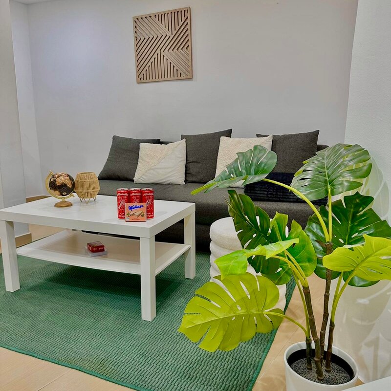 Helles Wohnzimmer mit Monstera & grünem Teppich – 2-Zimmer Wohnung zur Kurzzeitmiete, Wohnen auf Zeit 1 bis 6 Monate, Wien