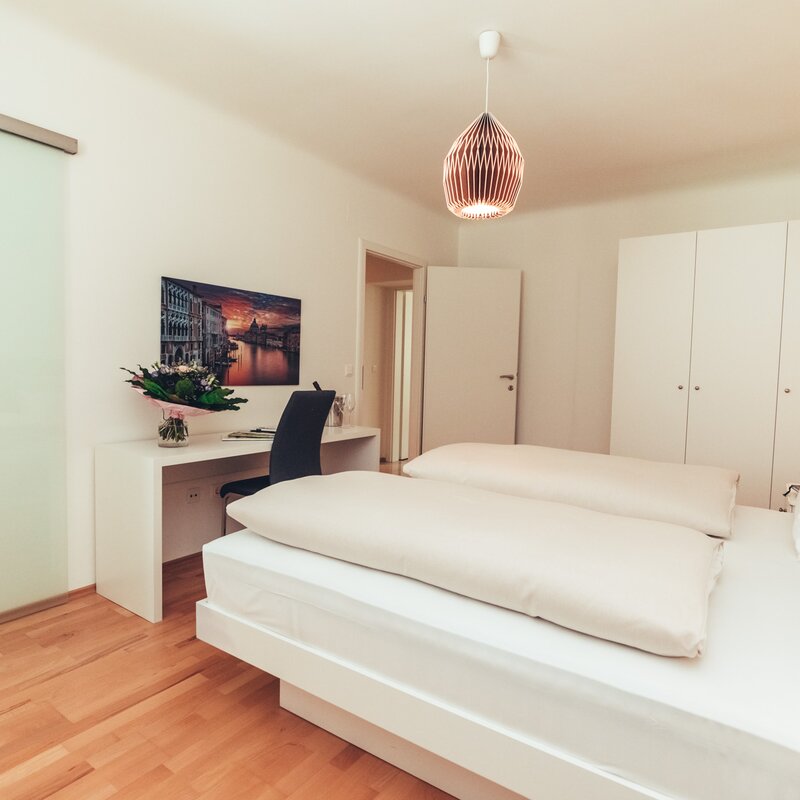 Schlafzimmer mit Schreibtisch, links Schiebetür zum Bad