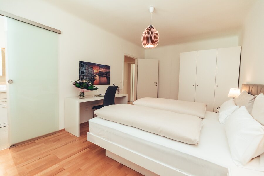 Schlafzimmer mit Schreibtisch, links Schiebetür zum Bad