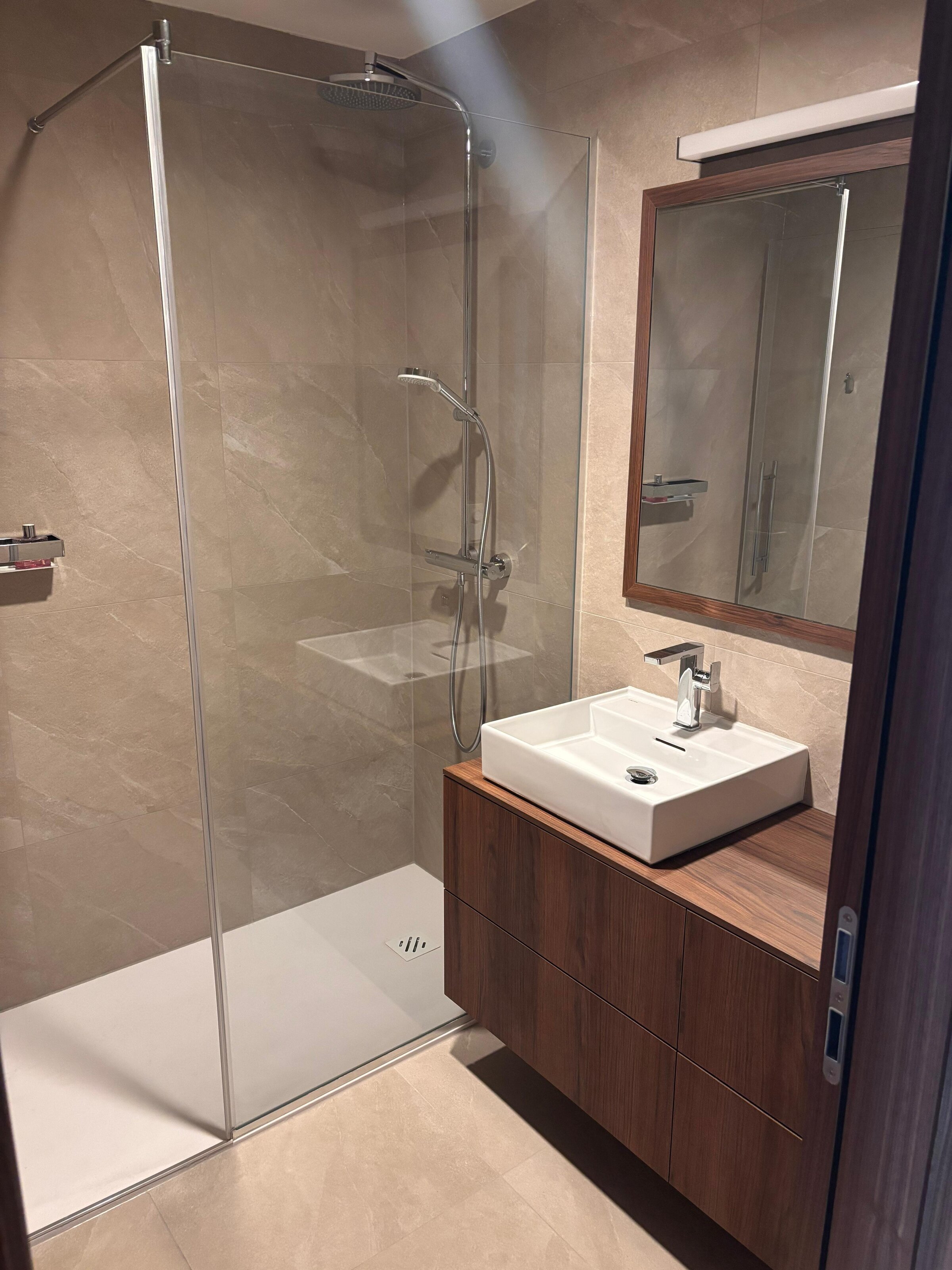 Das Bad ist hochwertig und modern ausgestattet und verfügt über elegante Steingutfliesen, ein Waschbecken von Laufen, maßgefertigte Tischlermöbel sowie eine großzügige Walk-in-Dusche. Die abgestimmten Materialien und die klare Gestaltung schaffen eine ruhige, hochwertige Atmosphäre.