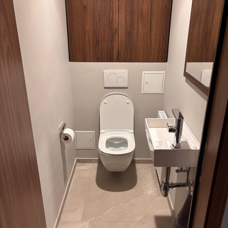 Das separate WC ist ebenfalls hochwertig gestaltet und mit Steingutfliesen, moderner Designsanitärausstattung sowie einem maßgefertigten Tischlerregal ausgestattet. Die klare Gestaltung fügt sich harmonisch in das hochwertige Gesamtkonzept der Wohnung ein.