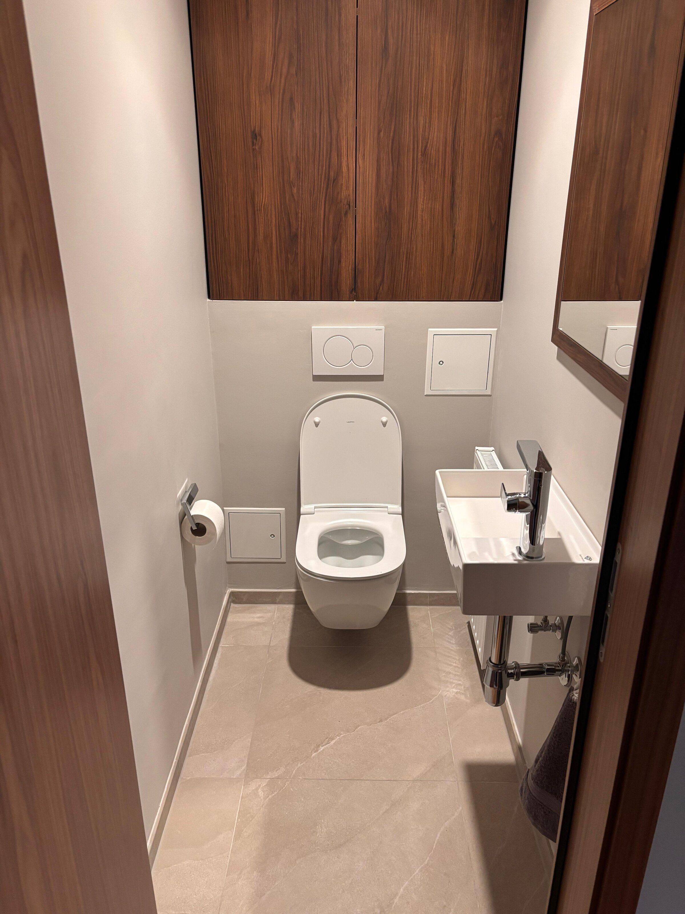 Das separate WC ist ebenfalls hochwertig gestaltet und mit Steingutfliesen, moderner Designsanitärausstattung sowie einem maßgefertigten Tischlerregal ausgestattet. Die klare Gestaltung fügt sich harmonisch in das hochwertige Gesamtkonzept der Wohnung ein.