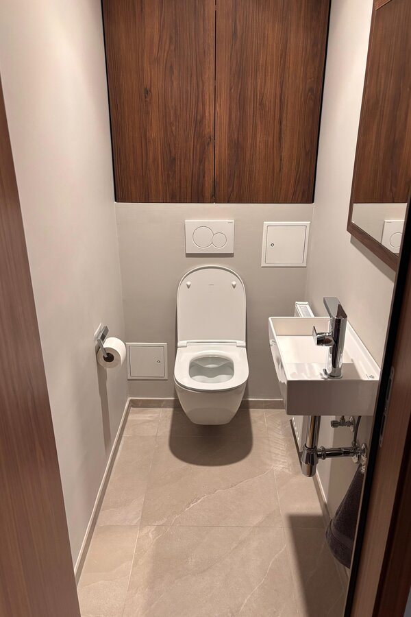 Das separate WC ist ebenfalls hochwertig gestaltet und mit Steingutfliesen, moderner Designsanitärausstattung sowie einem maßgefertigten Tischlerregal ausgestattet. Die klare Gestaltung fügt sich harmonisch in das hochwertige Gesamtkonzept der Wohnung ein.