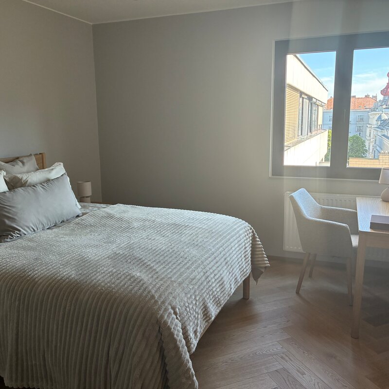 Das größere Schlafzimmer ist ruhig zur begrünten Innenruhelage ausgerichtet und bietet eine angenehme, entspannte Atmosphäre. Es ist hell, klar gestaltet und mit einem komfortablen Doppelbett, einem eigenen Schreibtisch sowie einem großzügigen Kleiderschrank ausgestattet. Dadurch eignet sich der Raum ideal für längere Aufenthalte und Homeoffice.