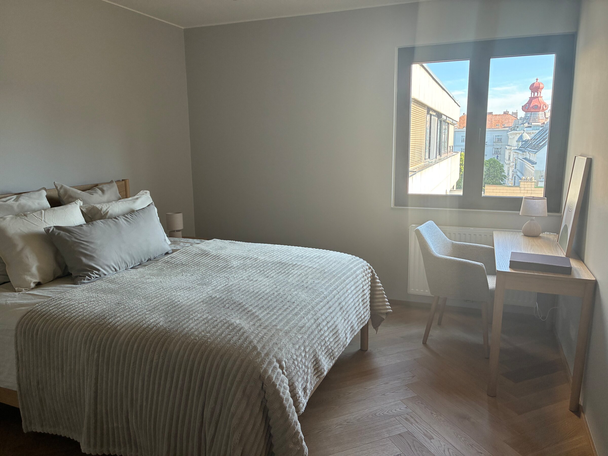Das größere Schlafzimmer ist ruhig zur begrünten Innenruhelage ausgerichtet und bietet eine angenehme, entspannte Atmosphäre. Es ist hell, klar gestaltet und mit einem komfortablen Doppelbett, einem eigenen Schreibtisch sowie einem großzügigen Kleiderschrank ausgestattet. Dadurch eignet sich der Raum ideal für längere Aufenthalte und Homeoffice.