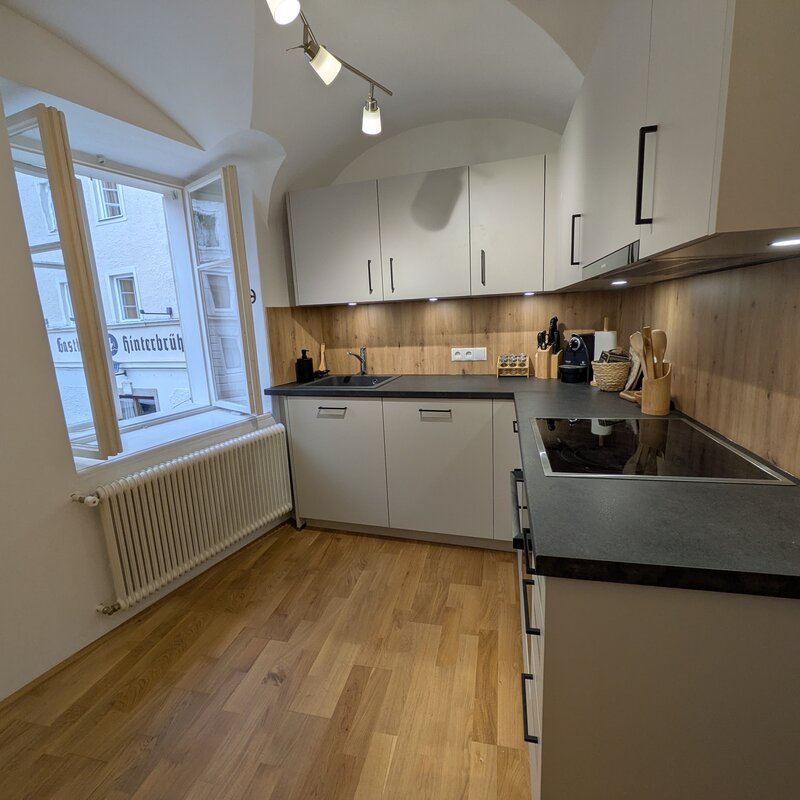Eine hochwertige Küche mit warmen Holzelementen, modernen Geräten und viel Tageslicht – perfekt für kulinarische Momente im Herzen der Stadt.