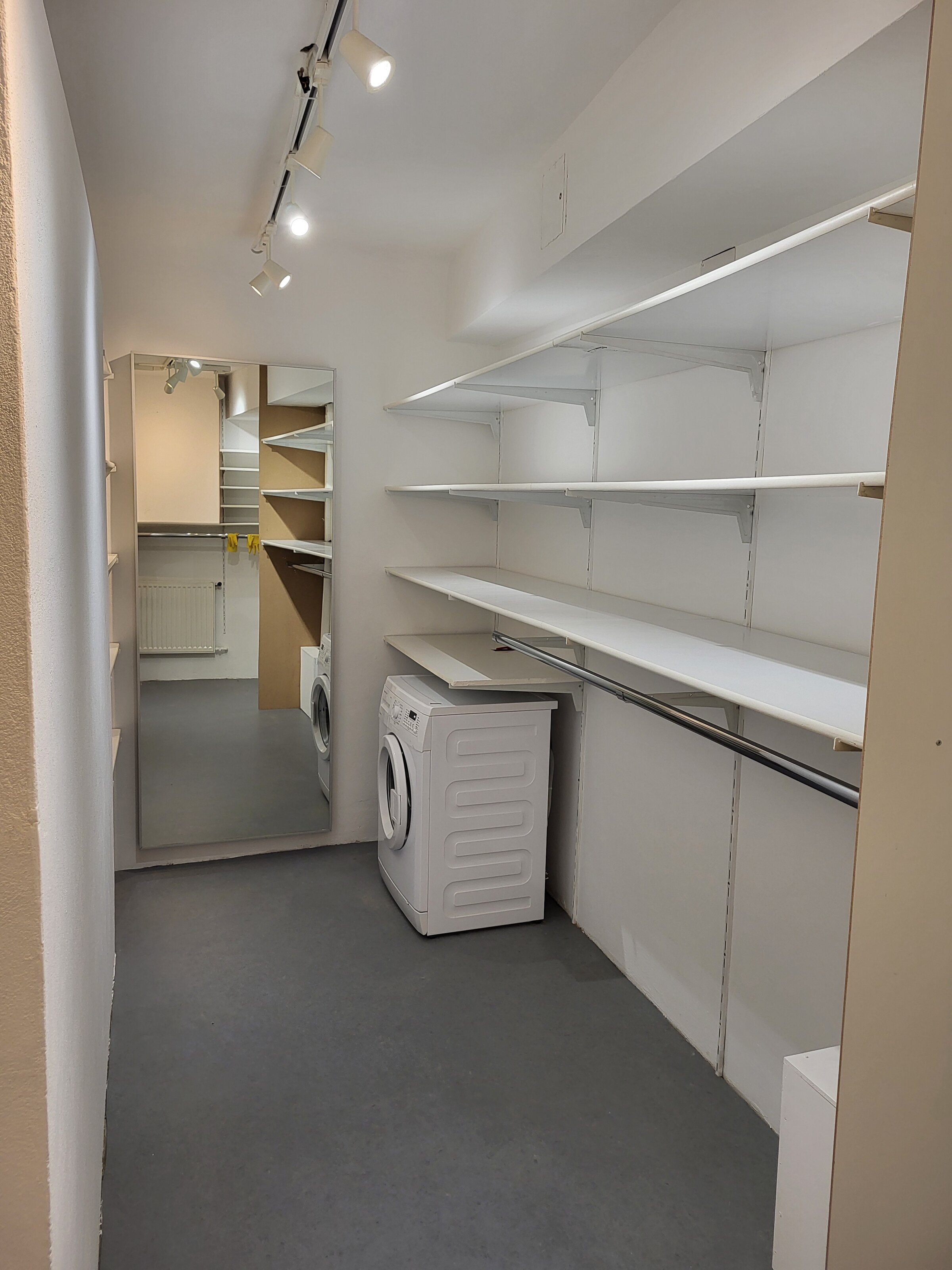 Ein großzügiger, klar strukturierter begehbarer Schrank mit offenen Regalen, großem Spiegel und integrierter Waschmöglichkeit – praktisch, modern und perfekt organisiert. | © Vermieter