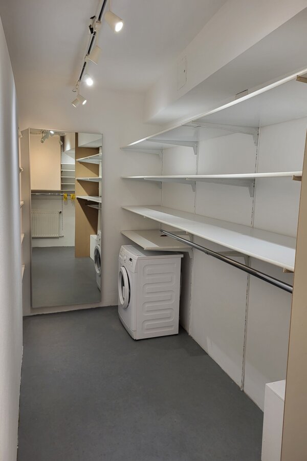 Ein großzügiger, klar strukturierter begehbarer Schrank mit offenen Regalen, großem Spiegel und integrierter Waschmöglichkeit – praktisch, modern und perfekt organisiert. | © Vermieter