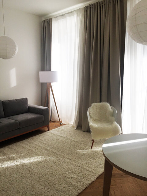 Wohnzimmer mit Sofa, Stehlampe, Stuhl, Fenster und separater Balkontür | © Jeanne Szilit