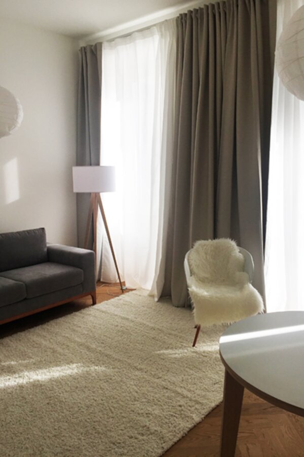 Wohnzimmer mit Sofa, Stehlampe, Stuhl, Fenster und separater Balkontür | © Jeanne Szilit