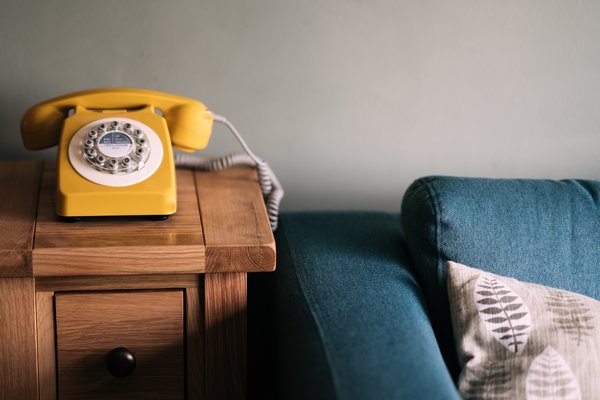 Gelbes Telefon mit Wählscheibe neben einer Couch | © Annie Spratt